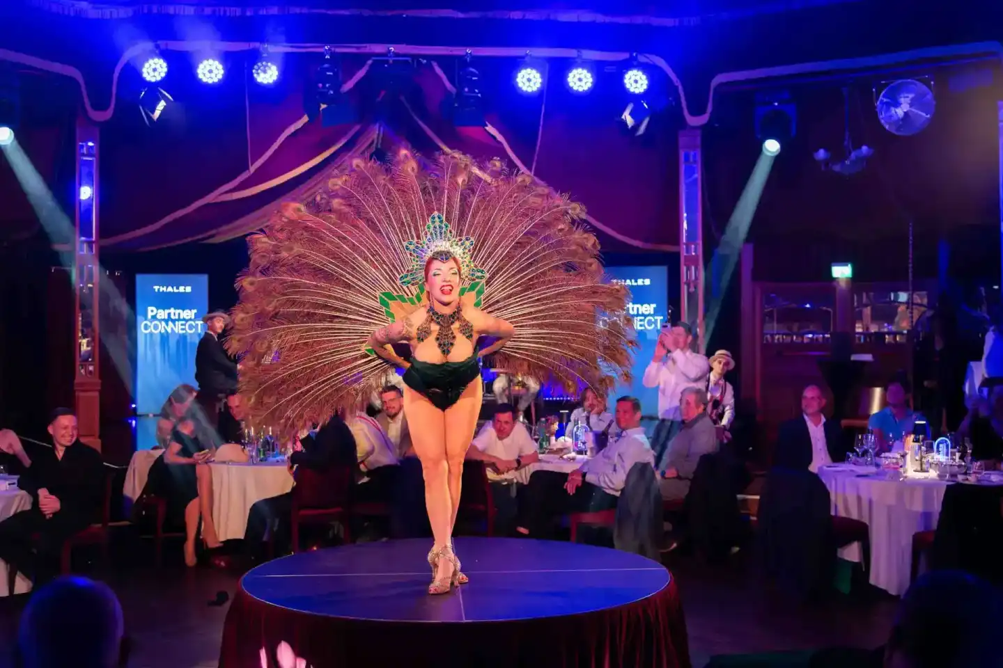Performerin in aufwendigem Federkostüm auf beleuchteter Bühne während Thales Firmenevent Wien