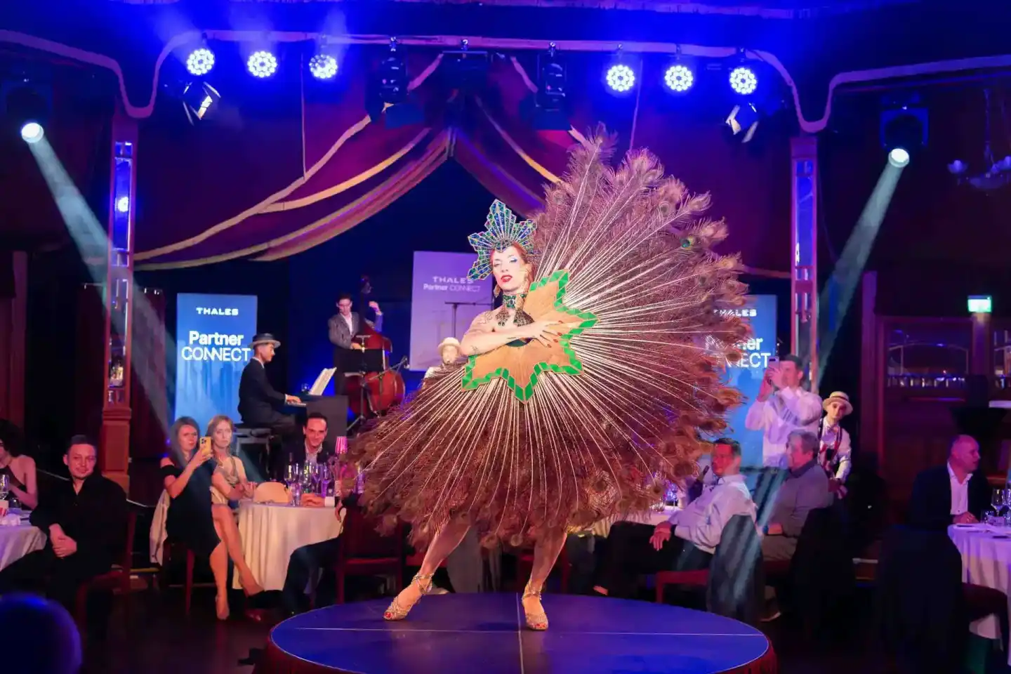 Showperformance bei Thales Partner Connect Event Wien: Künstlerin in opulenten Pfauenfedern-Kostüm auf Bühne vor Publikum