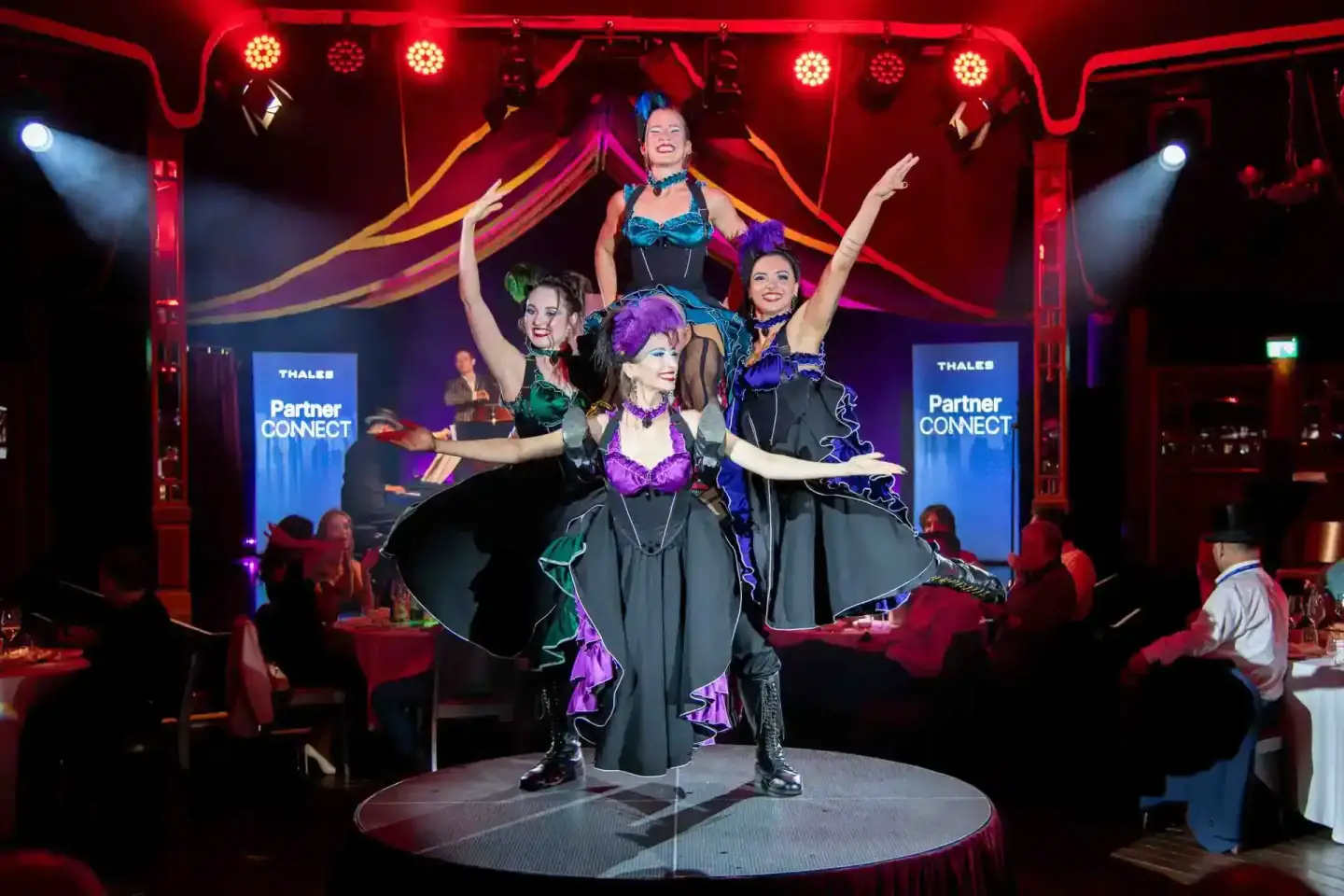 Vier Performerinnen in bunten Kostümen auf einer beleuchteten Bühne während eines Firmenevent Wien mit roter Lichtatmosphäre