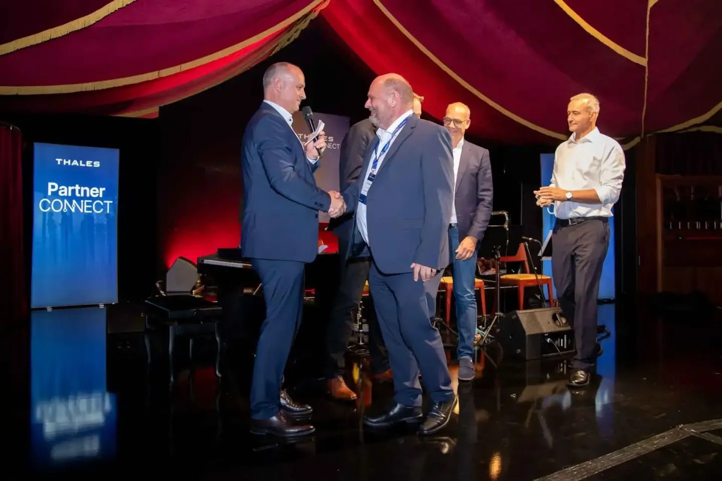 Eventfotograf Wien dokumentiert Geschäftsmänner beim Handschlag auf der Thales Partner Connect Veranstaltung unter rotem Bühn