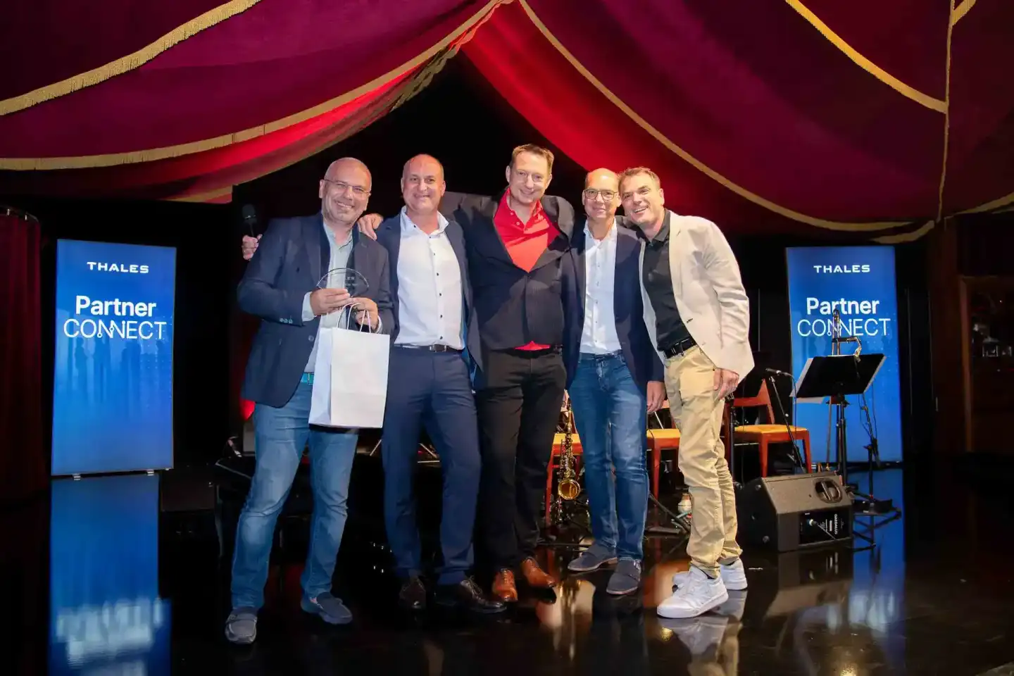 Fünf Geschäftsmänner posieren gemeinsam auf der Bühne beim Thales Partner Connect Event – professionelle Eventfotografie Wien
