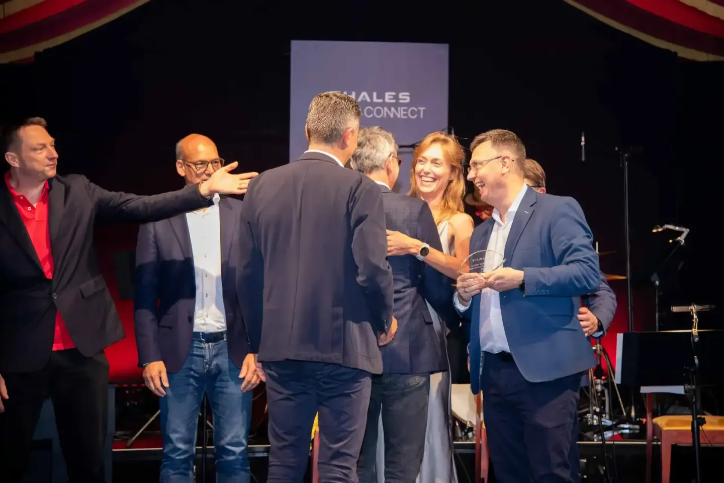 Teamfoto auf der Thales Connect Veranstaltung mit fünf Personen in Business-Kleidung, die lachend auf der Bühne stehen - prof