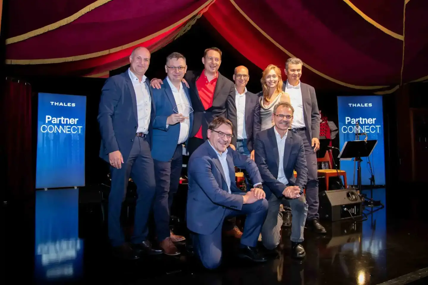 Teamfoto von acht Geschäftsleuten auf einer Bühne mit Thales Partner Connect Branding – professionelle Eventfotografie Wien