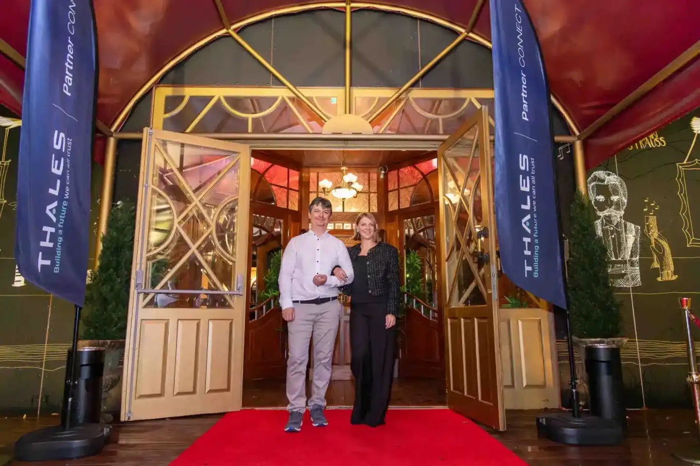 Zwei Personen stehen auf rotem Teppich vor elegantem Eingang beim Thales Firmenevent – professionelle Eventfotografie Wien