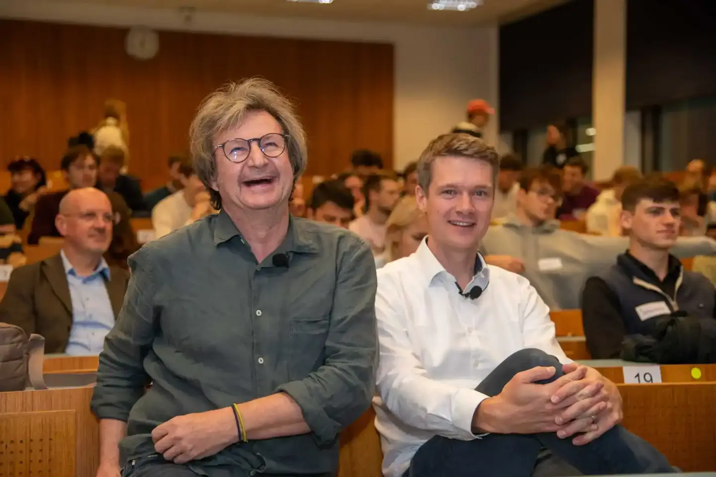 Zwei Männer sitzen lachend in einem Hörsaal bei einer Veranstaltung an der TU Wien, Eventfotografie Wien