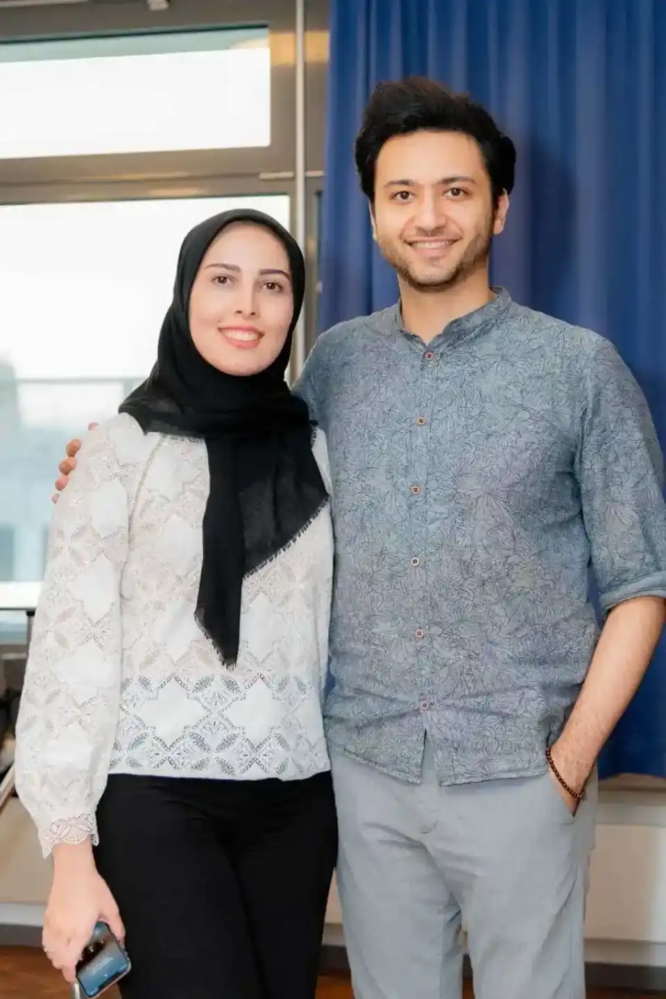 Zwei Personen posieren lächelnd vor blauen Vorhängen bei einem Firmenevent in Wien