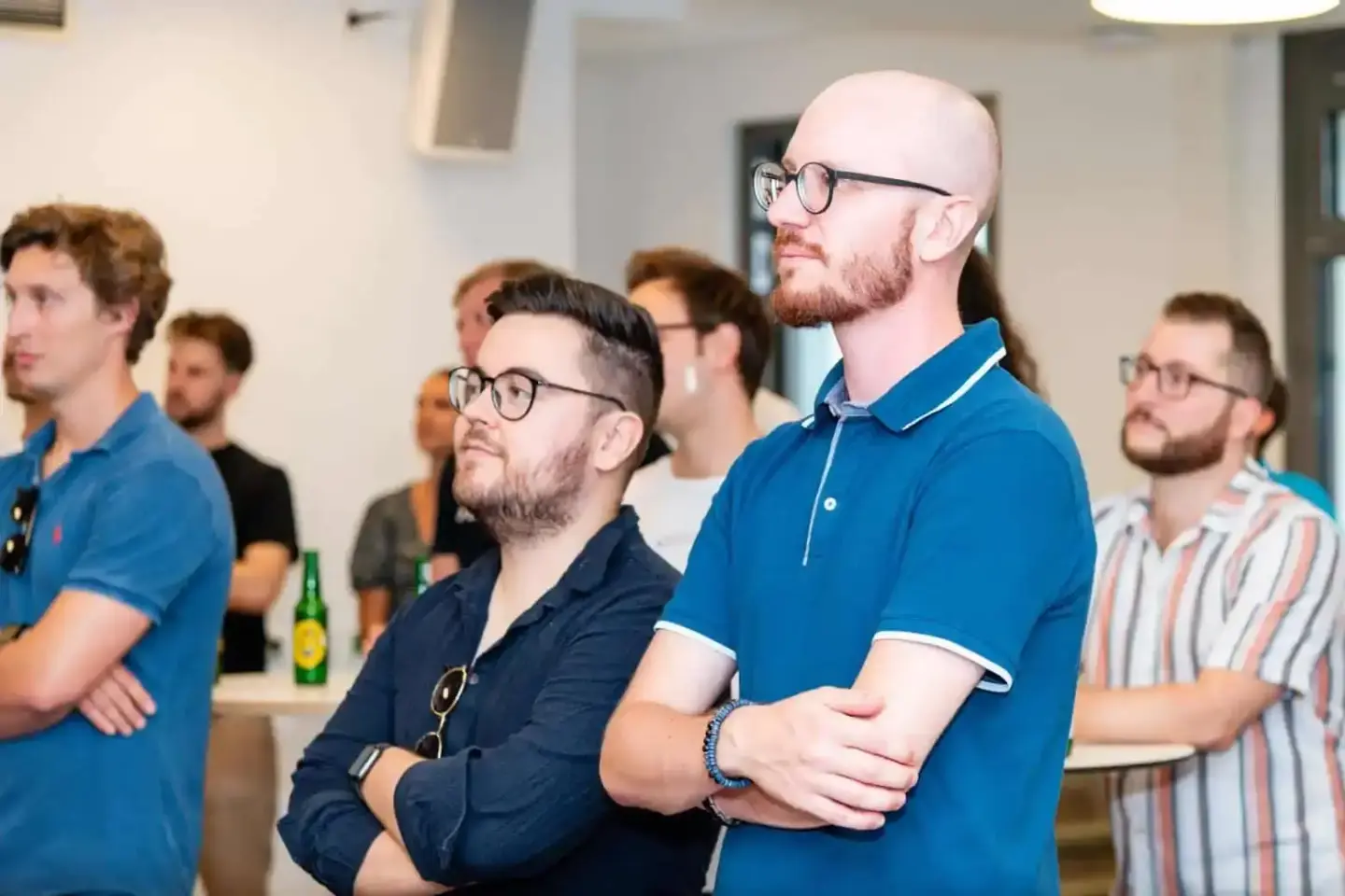 Gruppe von Männern bei einem Firmenevent in Wien, konzentriert auf Präsentation, mit Getränken im Hintergrund