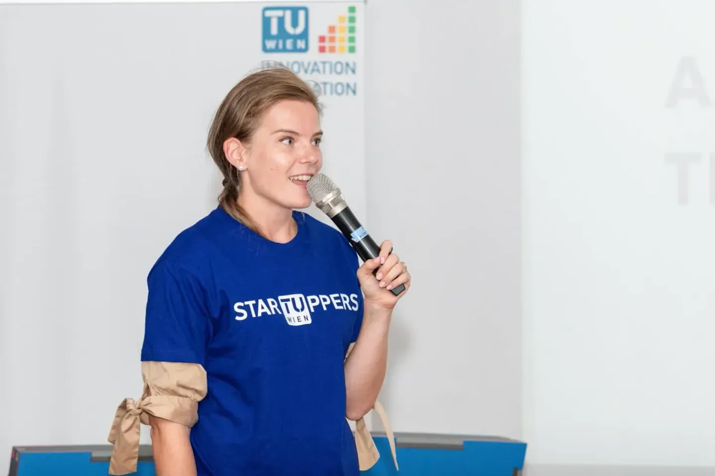 Junge Frau in blauem Startuppers Wien T-Shirt spricht mit Mikrofon auf TU Wien Veranstaltung - Eventfotograf Wien