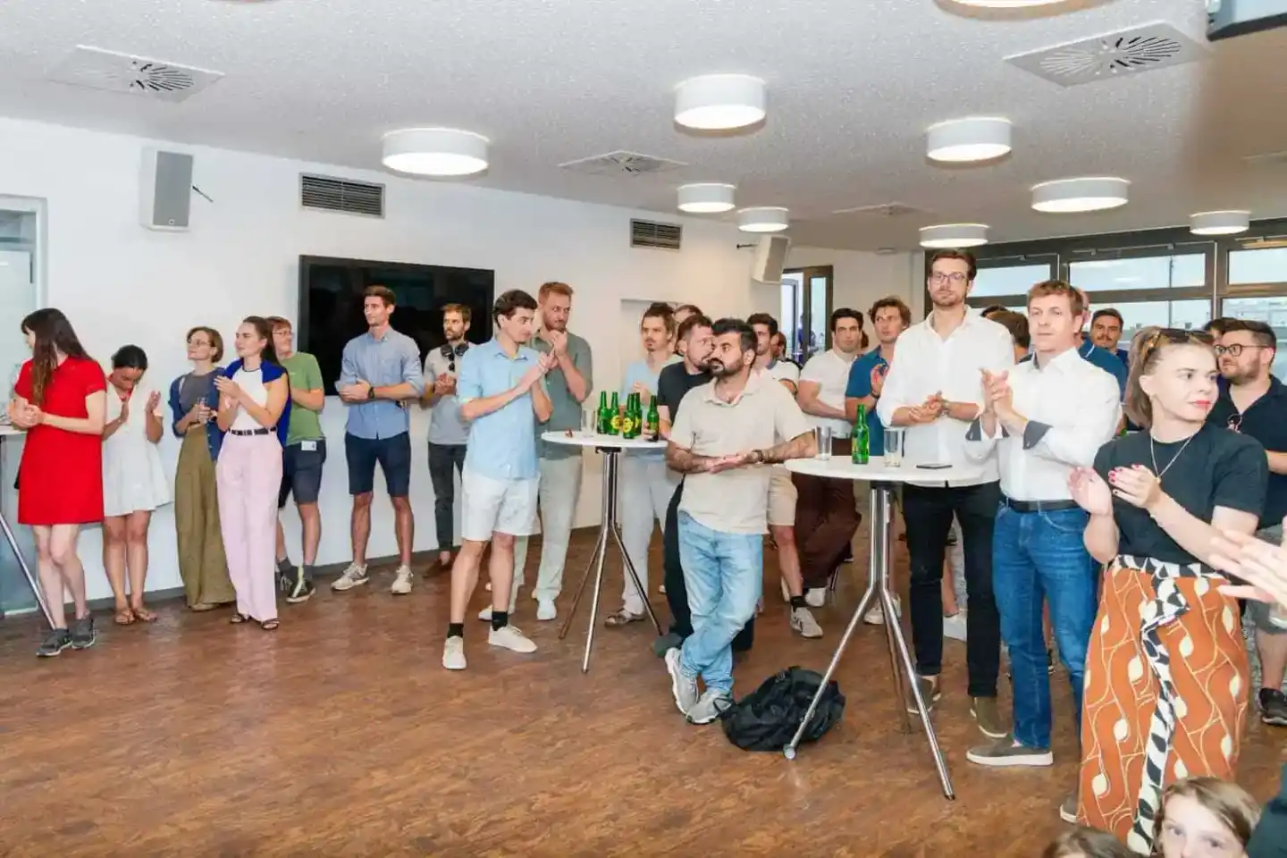 Große Gruppe von Gästen steht in modernem Veranstaltungsraum beim Firmenevent Wien, manche applaudieren, Getränke auf Stehtis