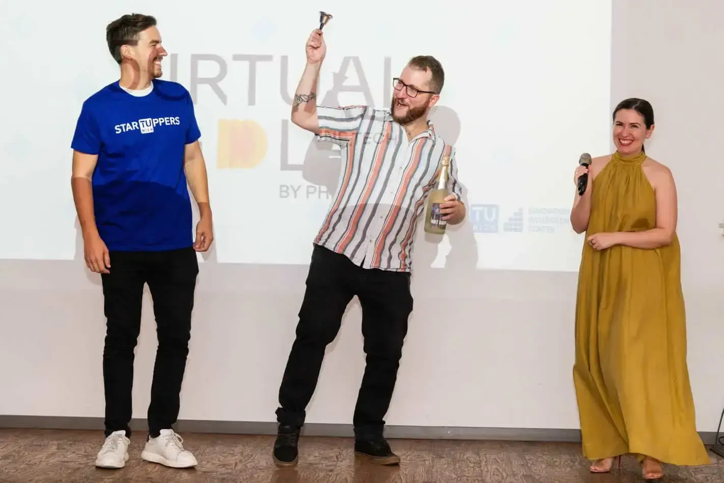 Drei Personen auf einer Bühne bei einer Veranstaltung an der TU Wien, der Mann in der Mitte hält einen Preis hoch