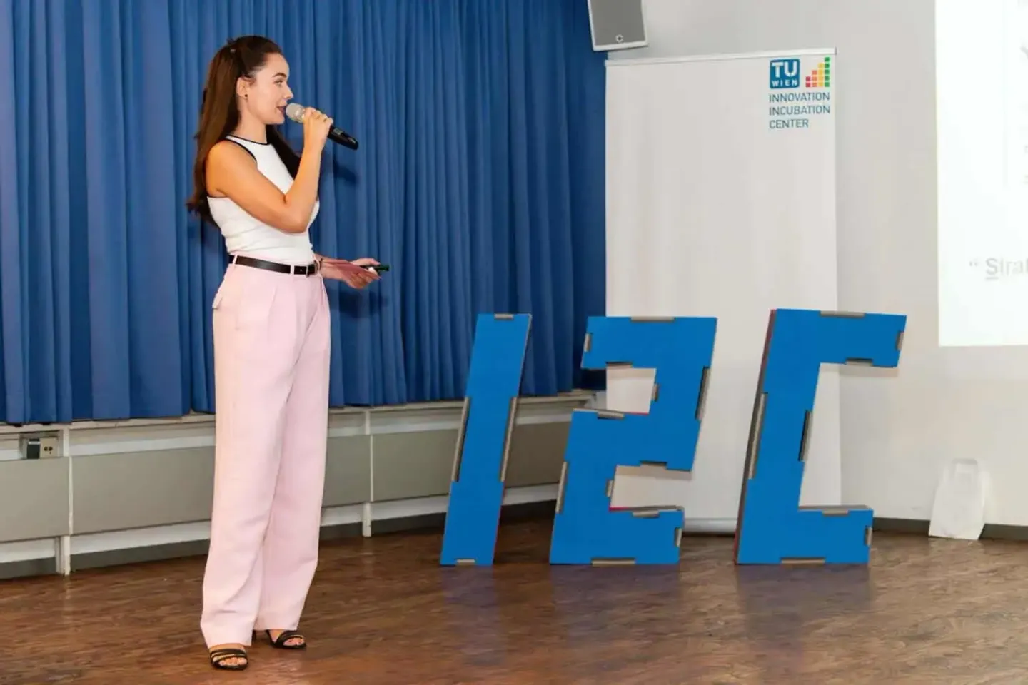 Rednerin spricht beim TU Wien Innovation Incubation Center Event mit Mikrofon vor blauem Vorhang