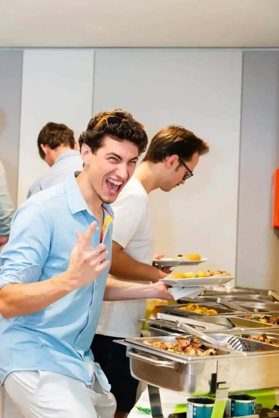 Junge Männer beim Buffet auf einem Firmenevent in Wien, lachend und essend