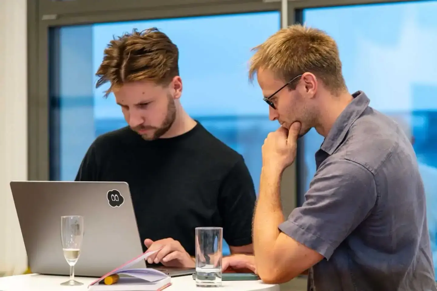 Zwei Männer diskutieren vor einem Laptop bei einem Firmenevent in Wien, mit Blick auf die Stadt im Hintergrund