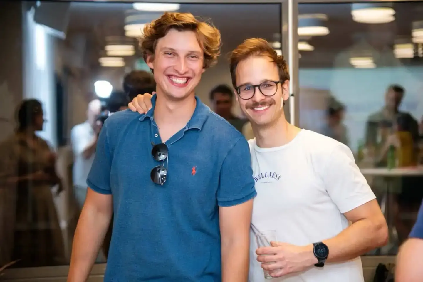 Zwei Männer posieren lächelnd auf einem Firmenevent Wien, einer trägt ein blaues Poloshirt mit Sonnenbrille, der andere ein w