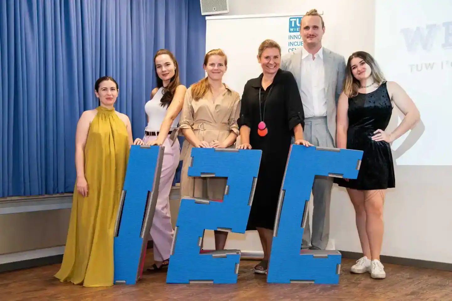 Team von sechs Personen posiert mit großen blauen Buchstaben bei einem Firmenevent der TU Wien, professionelle Eventfotografi