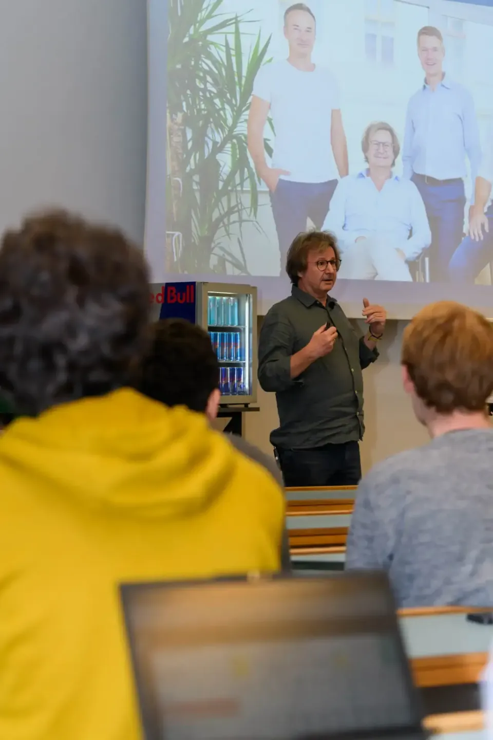Eventfotograf präsentiert vor Publikum an der TU Wien, im Hintergrund Teamfoto auf Projektionsfläche