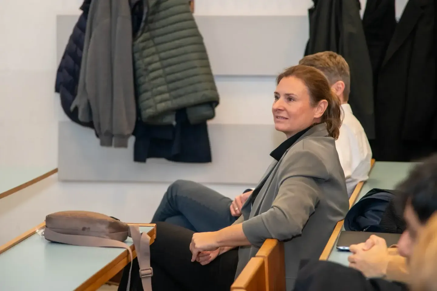 Teilnehmerin sitzt auf Holzbank während eines Firmenevent in Wien und verfolgt aufmerksam die Veranstaltung