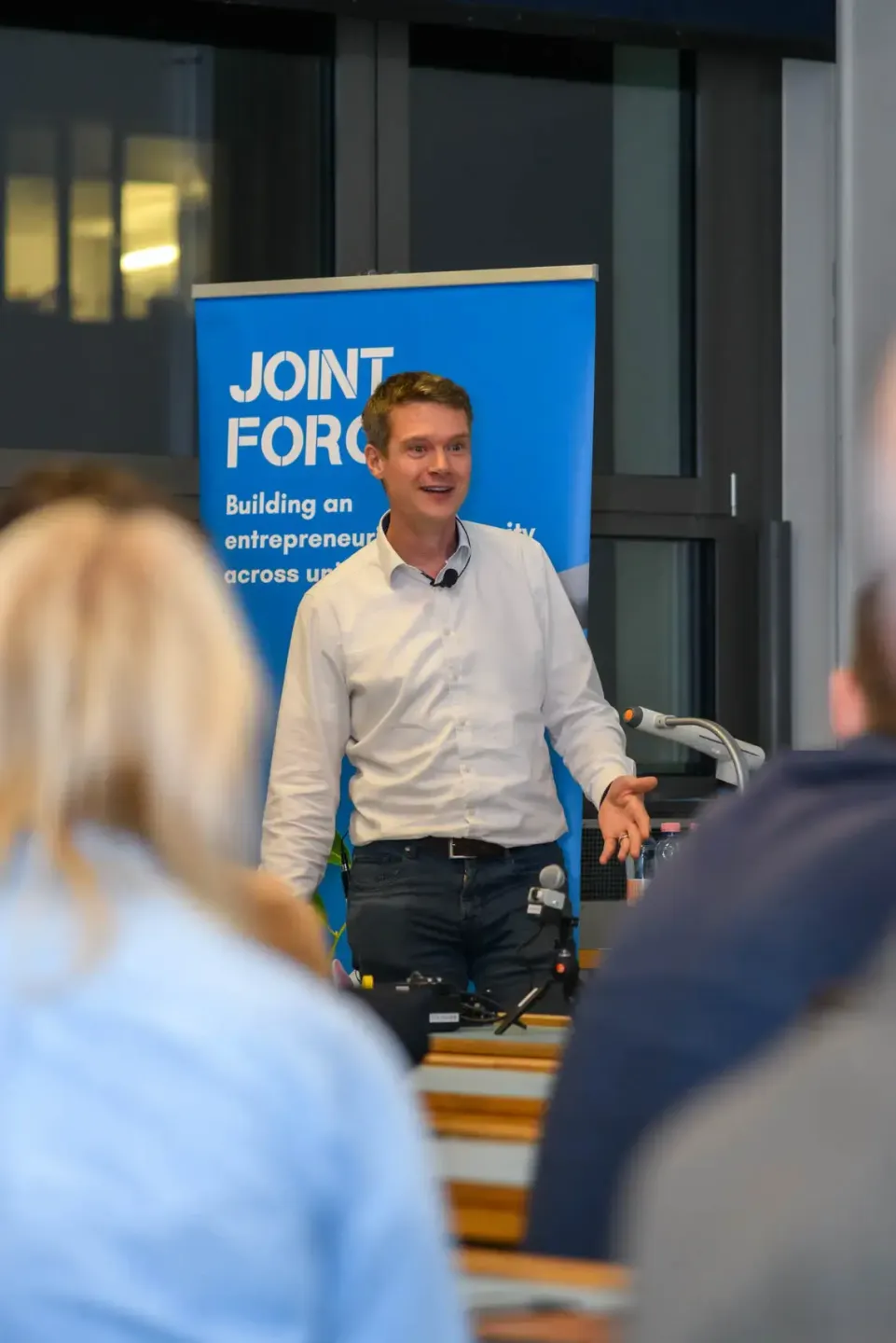 Junger Mann in weißem Hemd präsentiert beim TU Wien Event vor blauem Hintergrund mit Publikum im Vordergrund