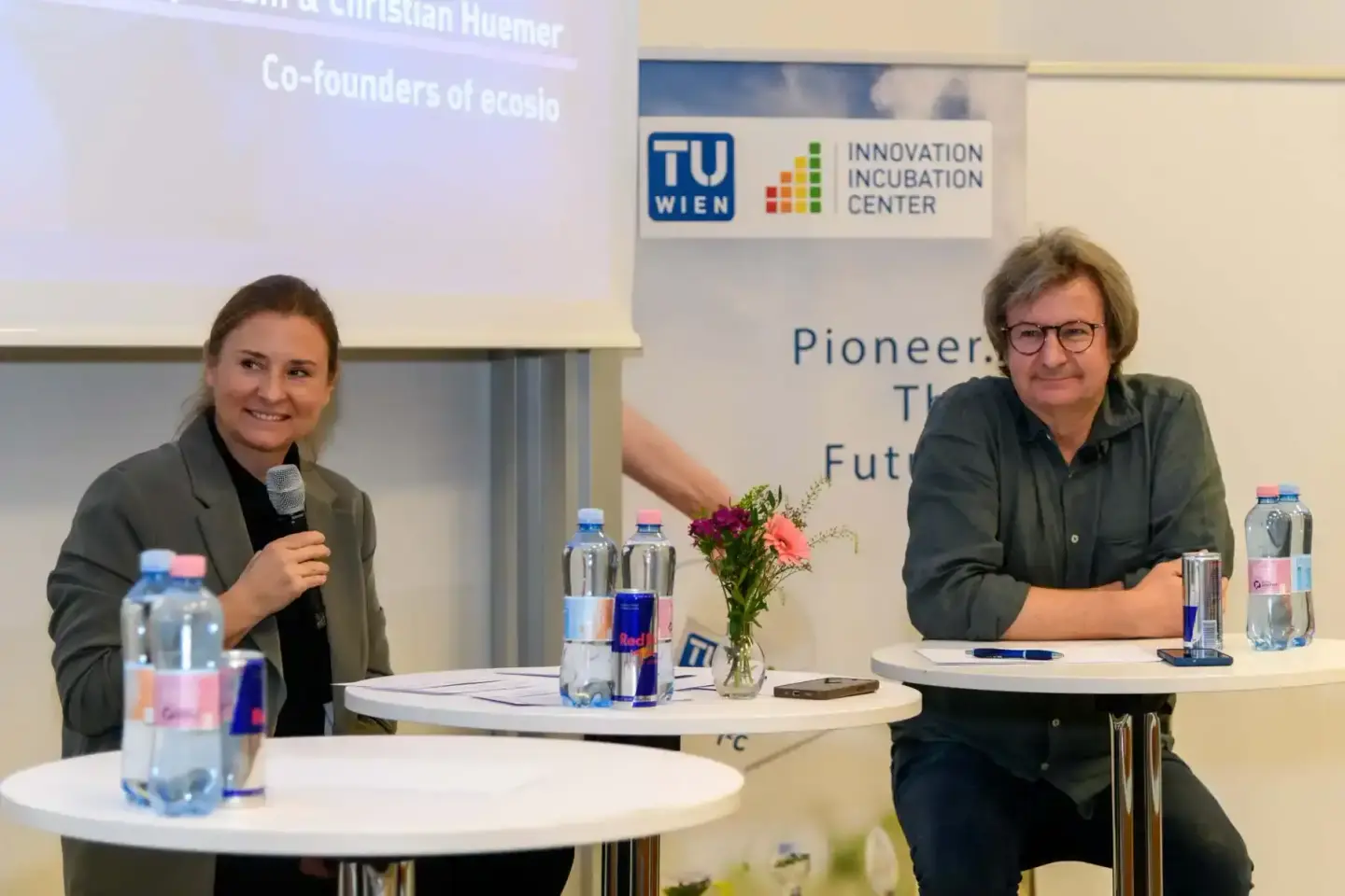 Zwei Sprecher bei einer Veranstaltung der TU Wien Innovation Incubation Center mit Mikrofon und Getränken am Podium