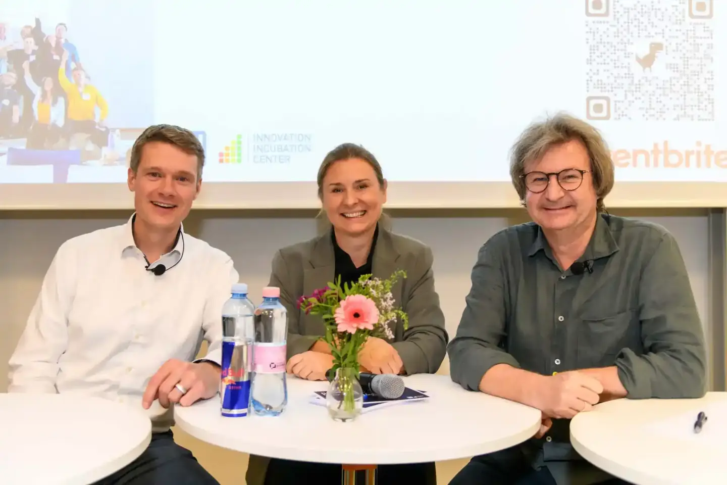 Drei Personen sitzen an einem Tisch bei einer Veranstaltung der TU Wien mit Mikrofon und Blumenstrauß - professionelle Eventf