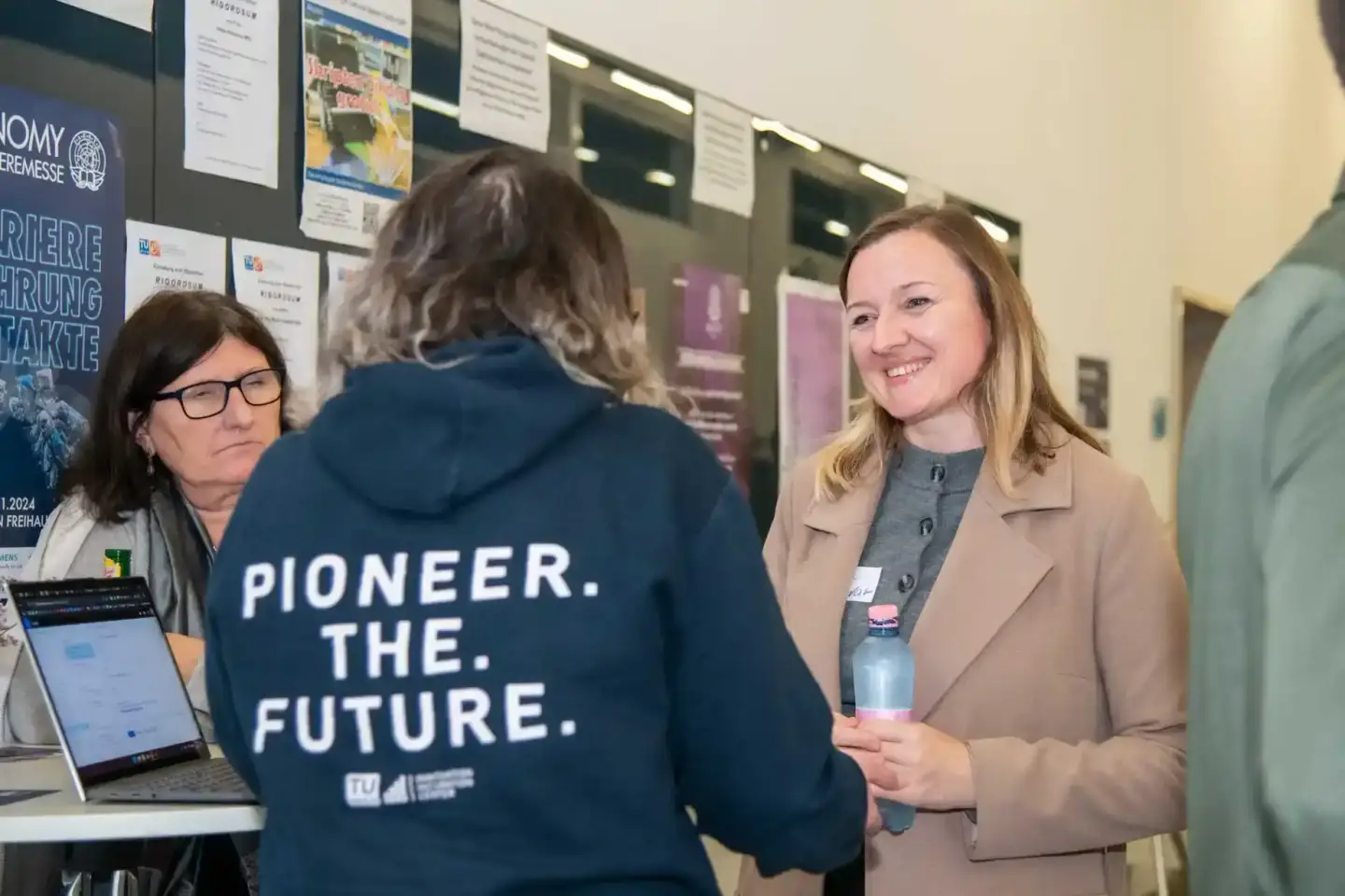 Eventfotografie Wien: Drei Personen im Gespräch bei einer TU Wien Veranstaltung, eine Frau in Beige-Blazer hält eine Wasserfl