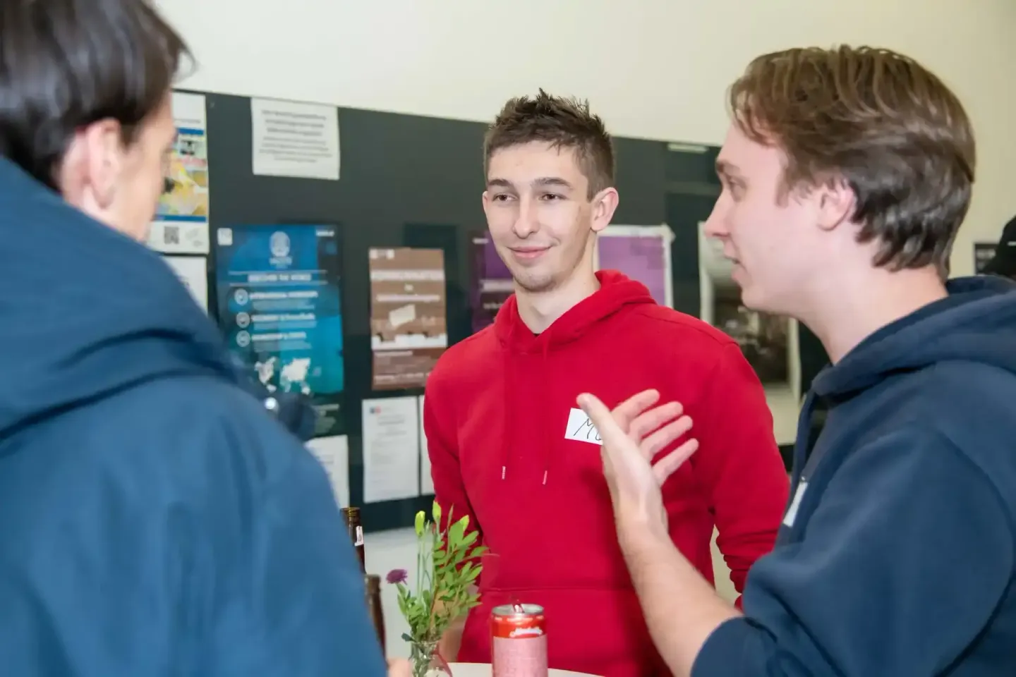 Junger Mann in rotem Hoodie präsentiert sein Projekt auf einer Veranstaltung der TU Wien vor zwei interessierten Besuchern