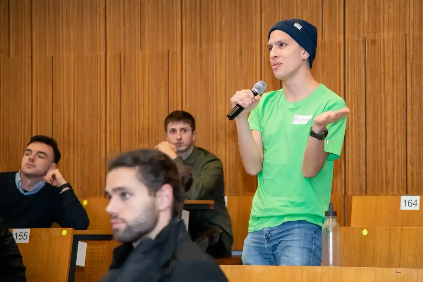 Eventfotograf dokumentiert Präsentation an der TU Wien: Sprecher in grünem Shirt mit Mikrofon vor Publikum im Hörsaal