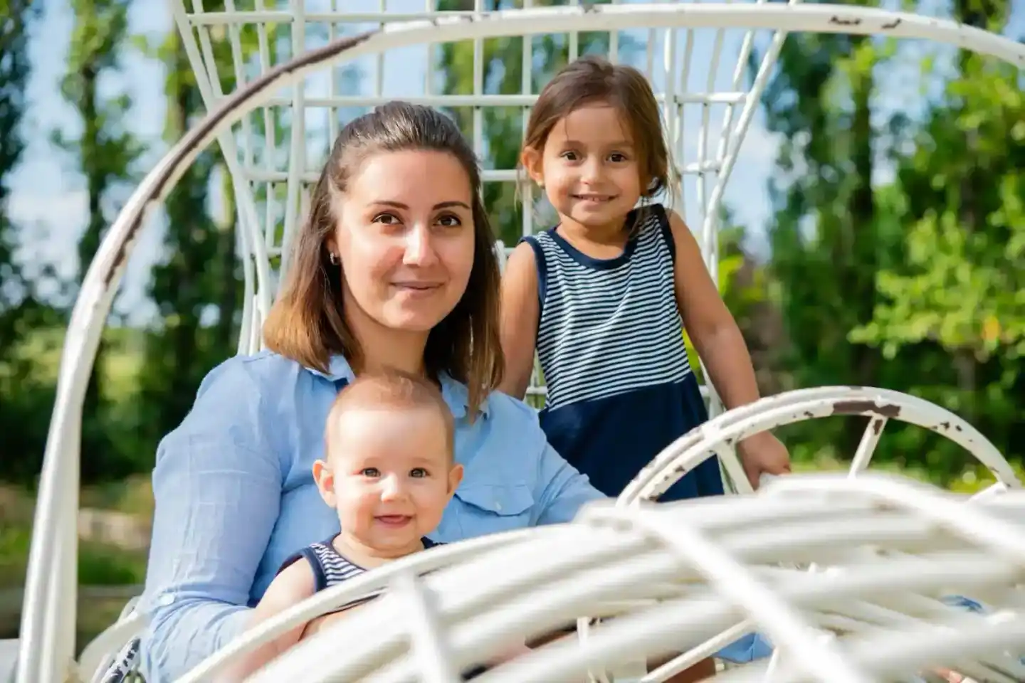 Mutter mit drei Kindern in gestreifter Kleidung im Garten vor weißem Rankgitter - Familienfotografie Wien
