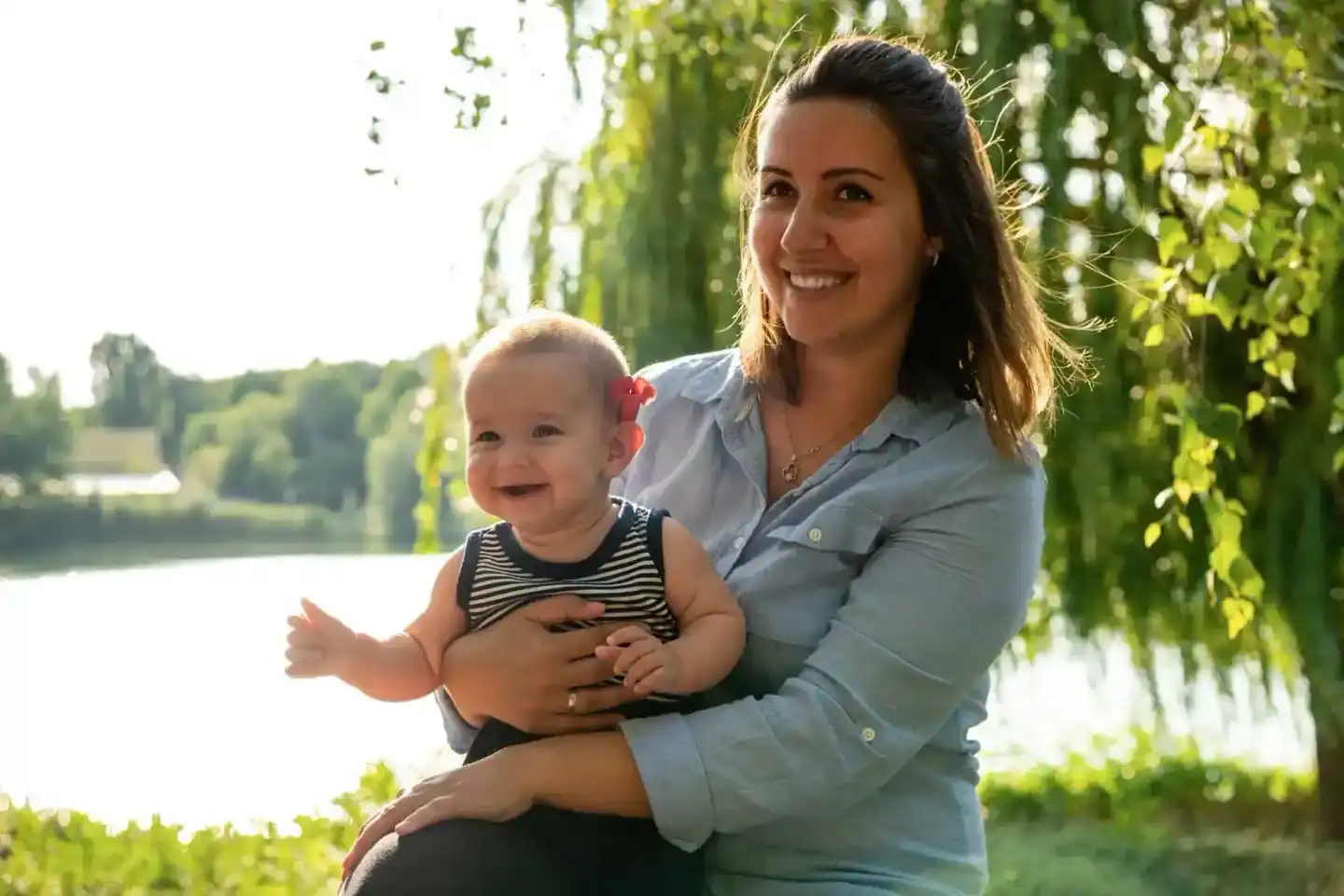 Mutter hält lachendes Baby am Flussufer unter Weidenbaum - professionelle Familienfotos Wien
