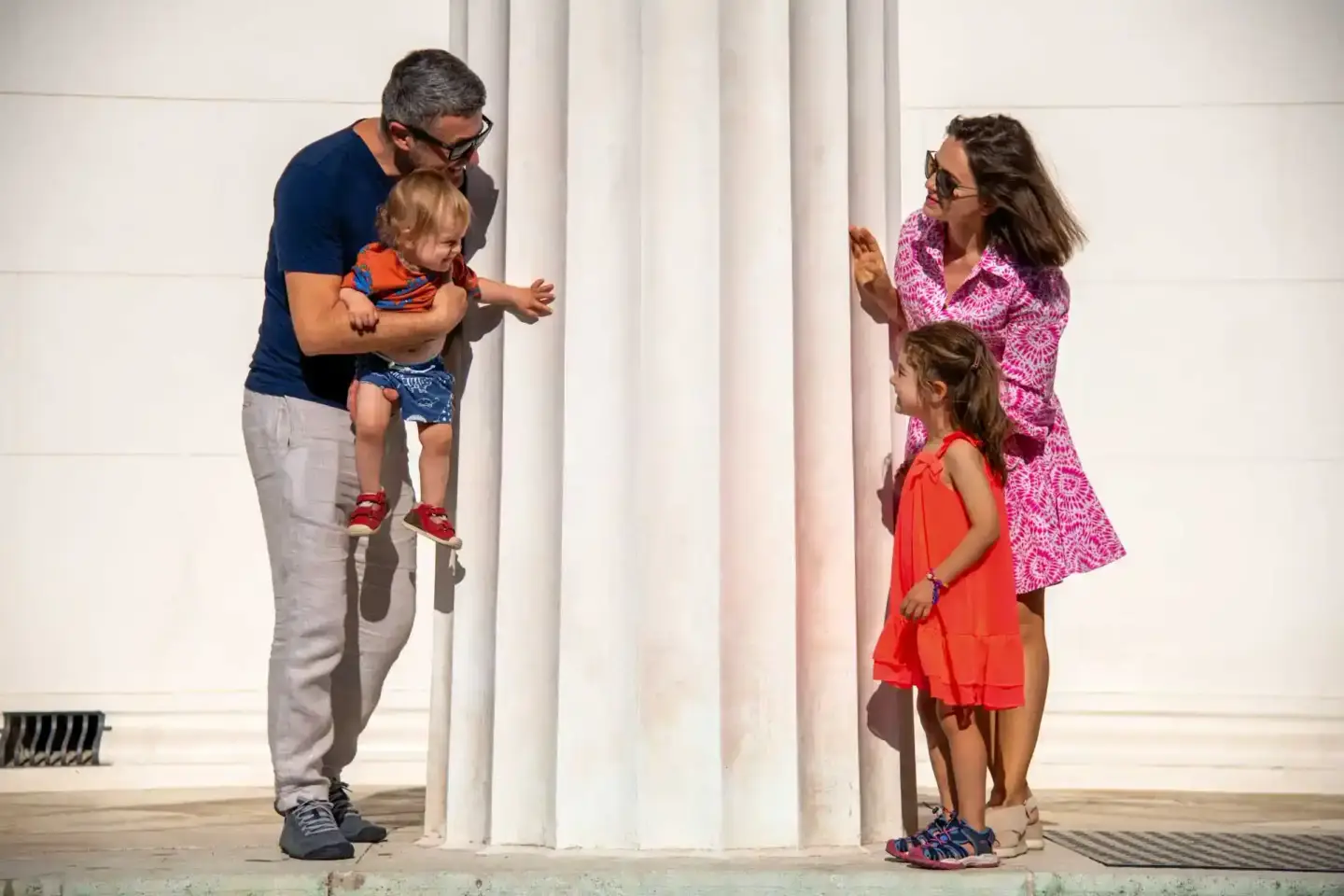 Familie mit zwei Kindern zwischen weißen Säulen, Vater hält Kleinkind, Mutter mit Tochter – Familienfotografie Wien