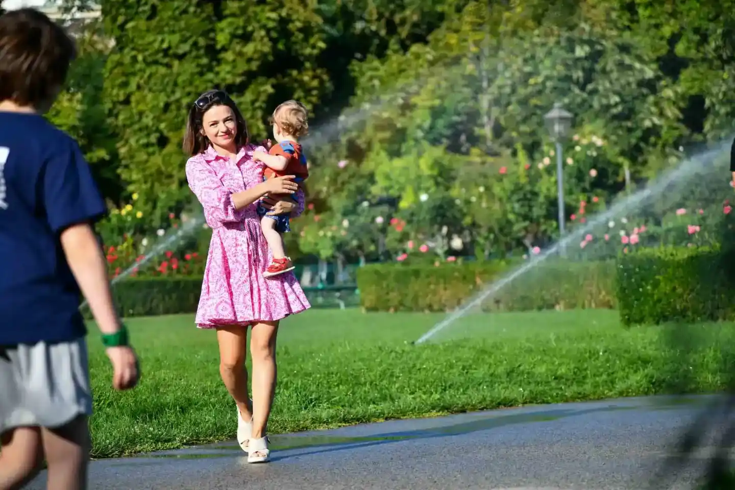 Mutter mit Kleinkind im grünen Garten, Familienfotografie Wien, Kind in Rot auf dem Arm