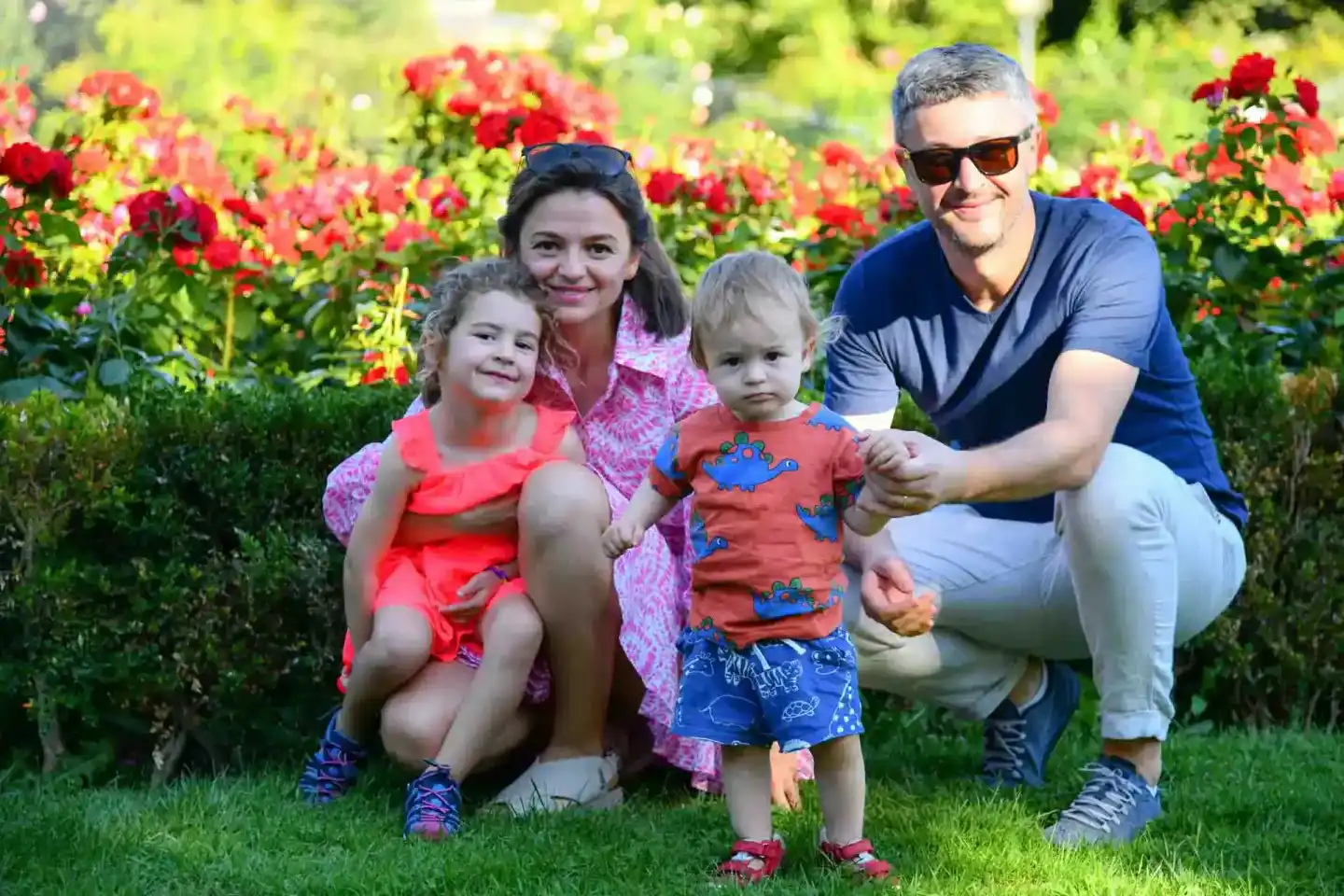 Familie mit zwei Kindern posiert lächelnd in einem Blumengarten mit roten Blüten – professionelle Familienfotografie Wien