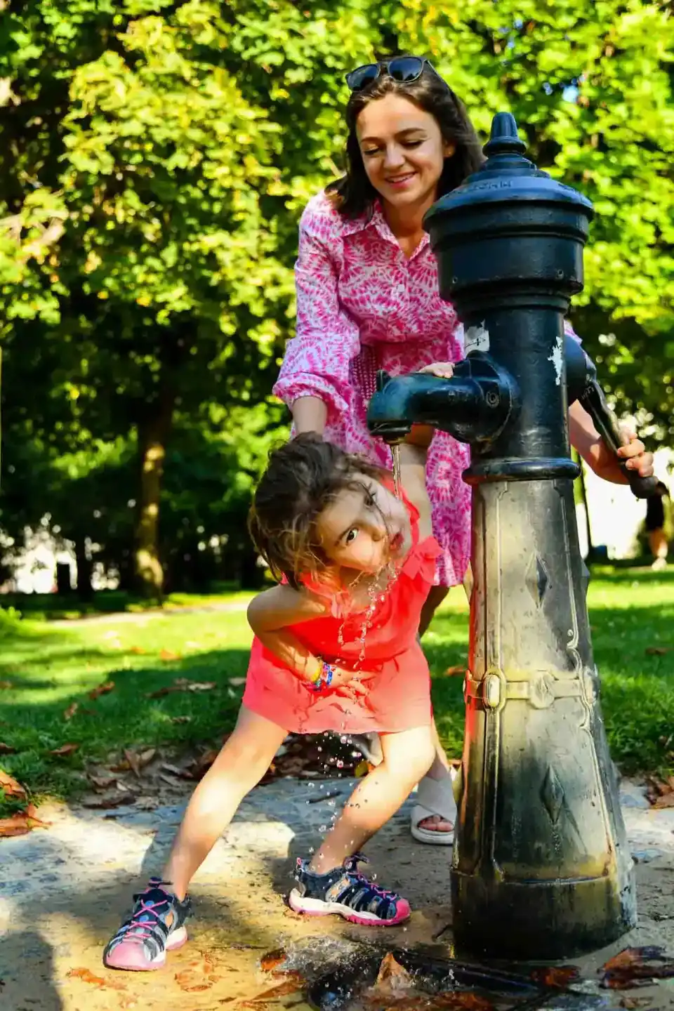 Mutter und kleines Kind spielen an einem öffentlichen Brunnen im Park - Familienfotografie Wien