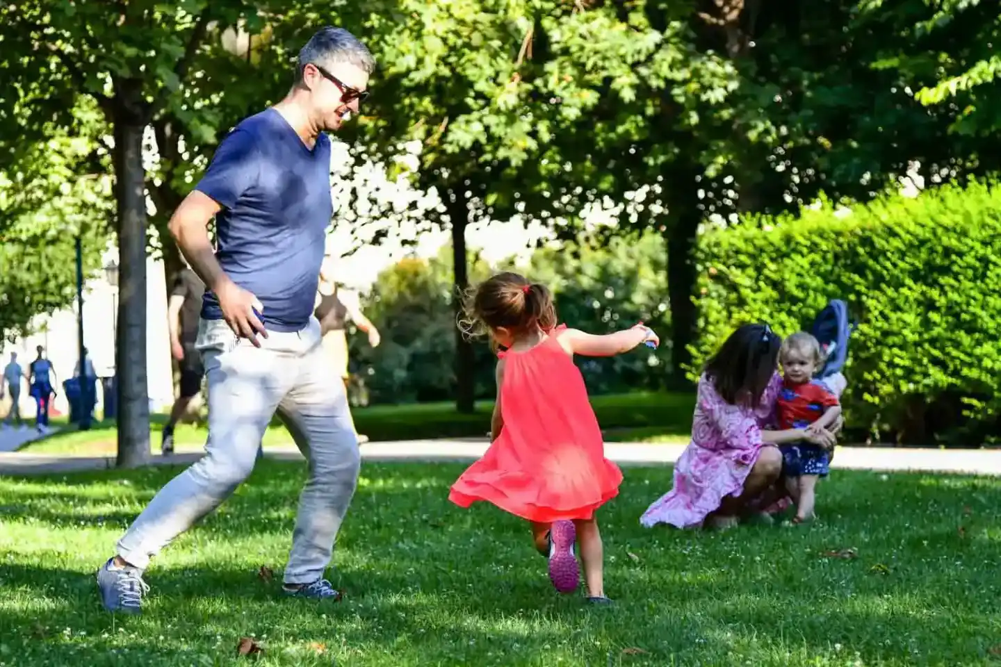 Vater spielt mit drei kleinen Kindern auf grüner Wiese im Park - Familienfotografie Wien