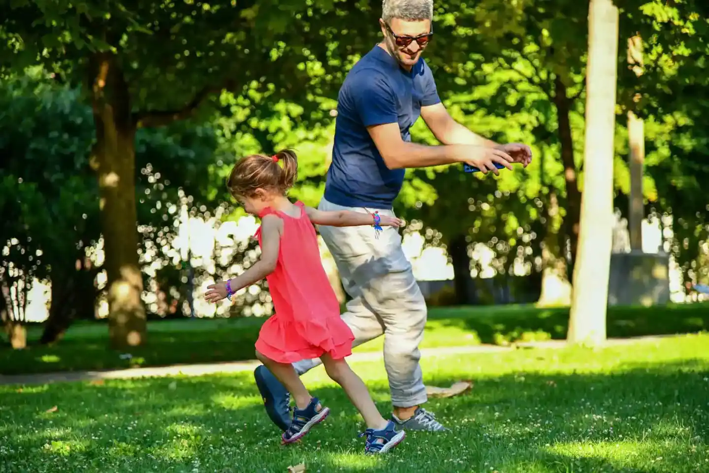 Vater und kleine Tochter tanzen zusammen im sonnigen Park – professionelle Familienfotografie Wien