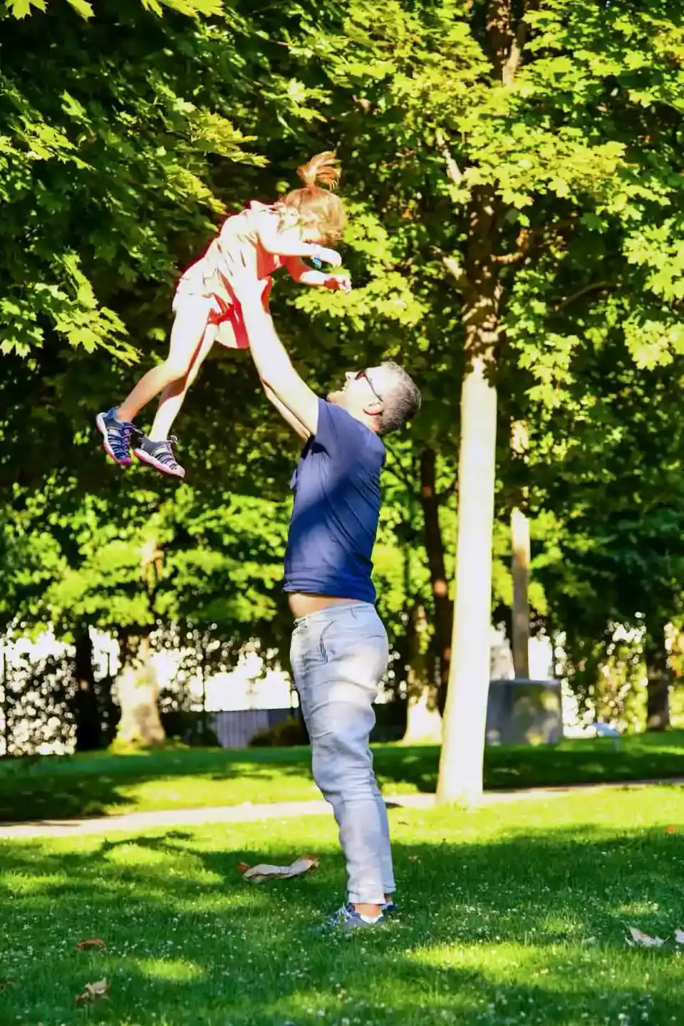 Vater wirft lachend sein Kind in die Luft im grünen Park – Familienfotografie Wien
