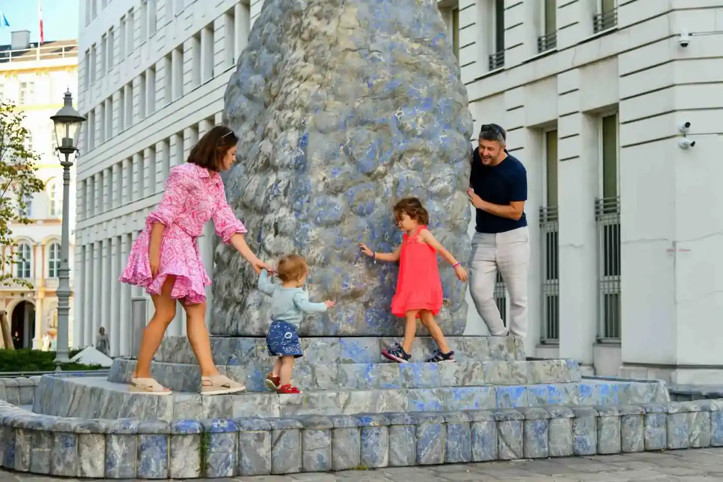 Familie mit zwei Kindern spielt an einem großen Steinmonument in Wien - Familienfotografie in der Stadt