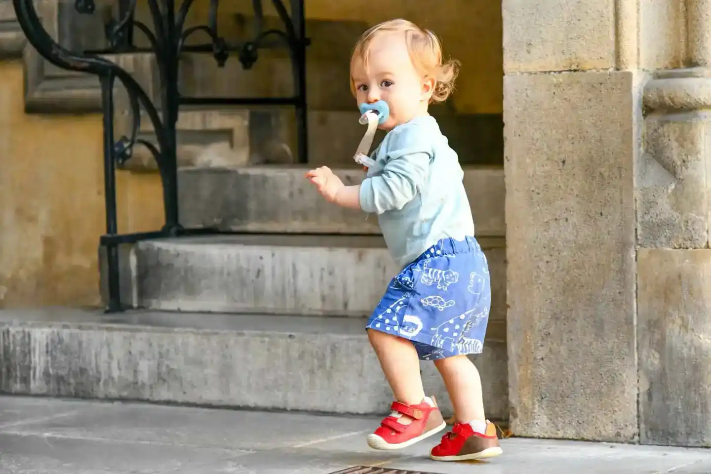 Kleines Kind mit blondem Lockenhaar läuft lachend in roten Sandalen über Kopfsteinpflaster einer Wiener Altstadt-Gasse