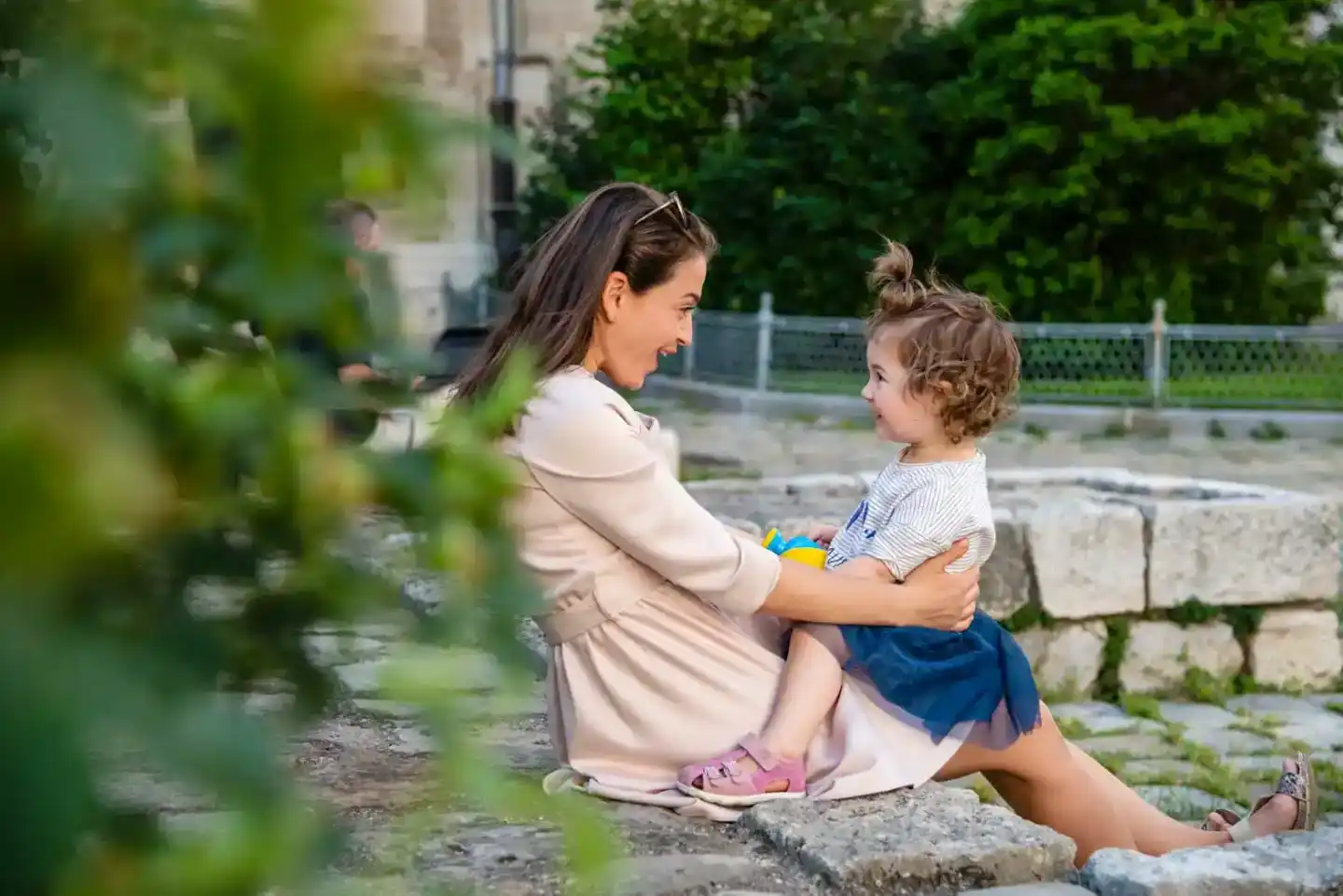 Mutter mit kleinem Kind sitzen zusammen auf Steinen in einem grünen Park - Familienfotografie Wien