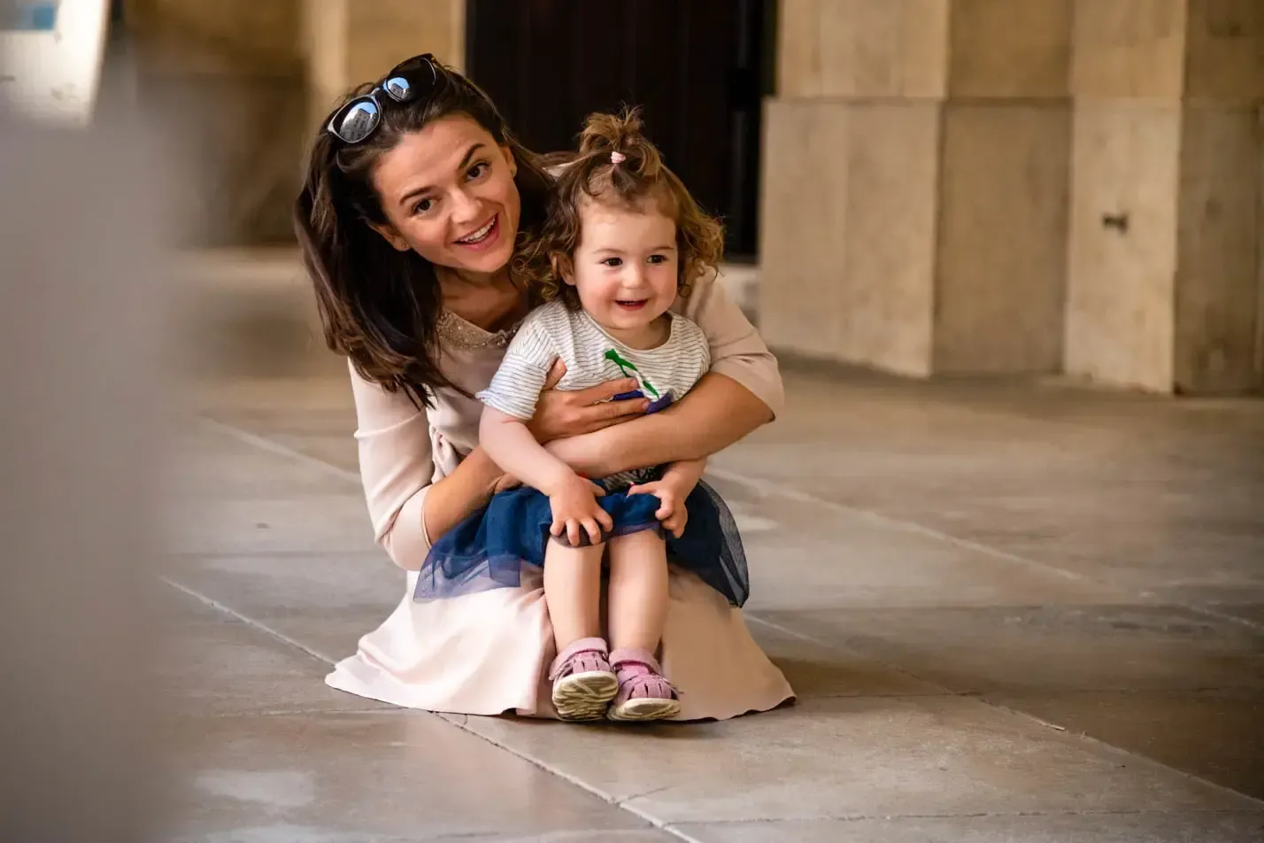 Mutter hält lächelndes Kleinkind auf dem Schoß in urbaner Umgebung – professionelle Familienfotografie Wien