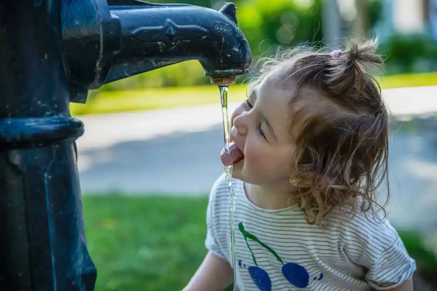 Kleines Mädchen trinkt aus einem öffentlichen Brunnen, Familienfotografie Wien