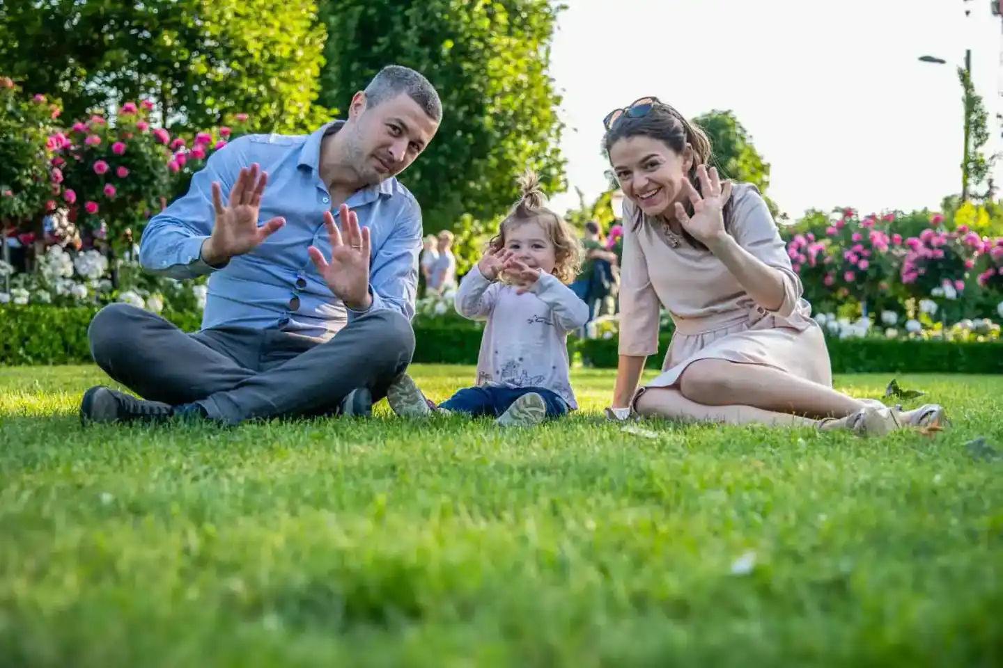 Glückliche Familie mit kleinem Kind sitzt lachend auf grüner Wiese in einem Garten mit bunten Blüten – professionelle Familie