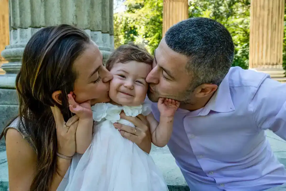 Glückliche Familie mit kleinem Kind beim Familienfotoshooting in Wien - Eltern küssen ihr lachendes Mädchen