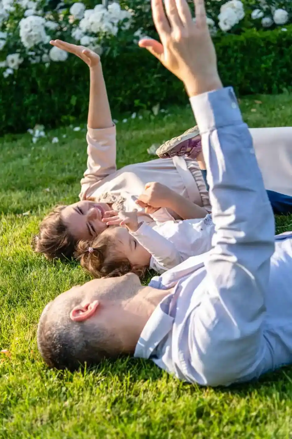 Glückliche Familie liegt lachend auf grüner Wiese mit weißen Blüten im Hintergrund – Familienfotografie Wien