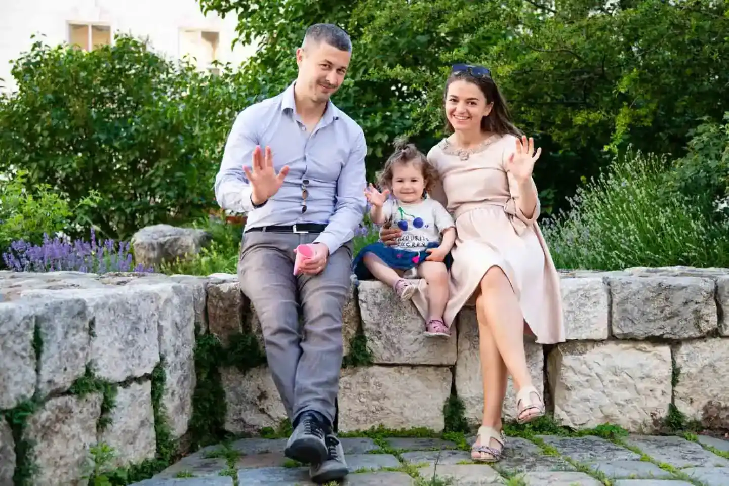 Glückliche Familie mit kleinem Kind sitzt auf einer Steinmauer im grünen Garten, professionelle Familienfotografie Wien