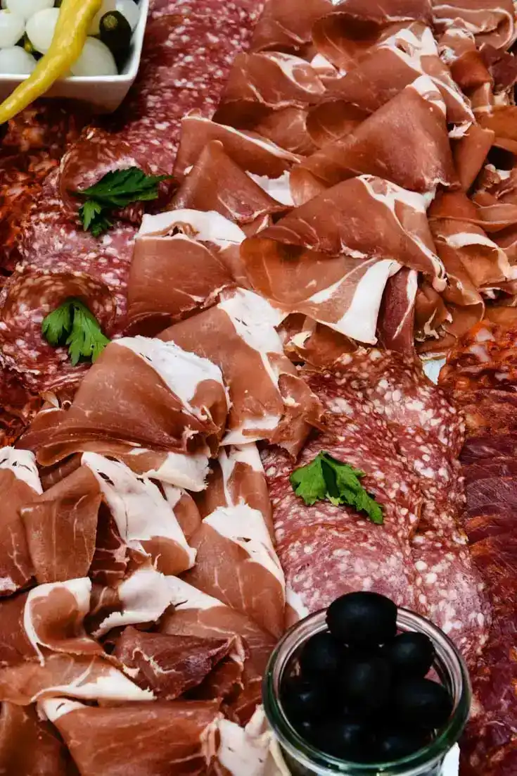 Appetitliche Charcuterie-Platte mit Prosciutto, Salami und schwarzen Oliven, professionell arrangiert mit Petersilie