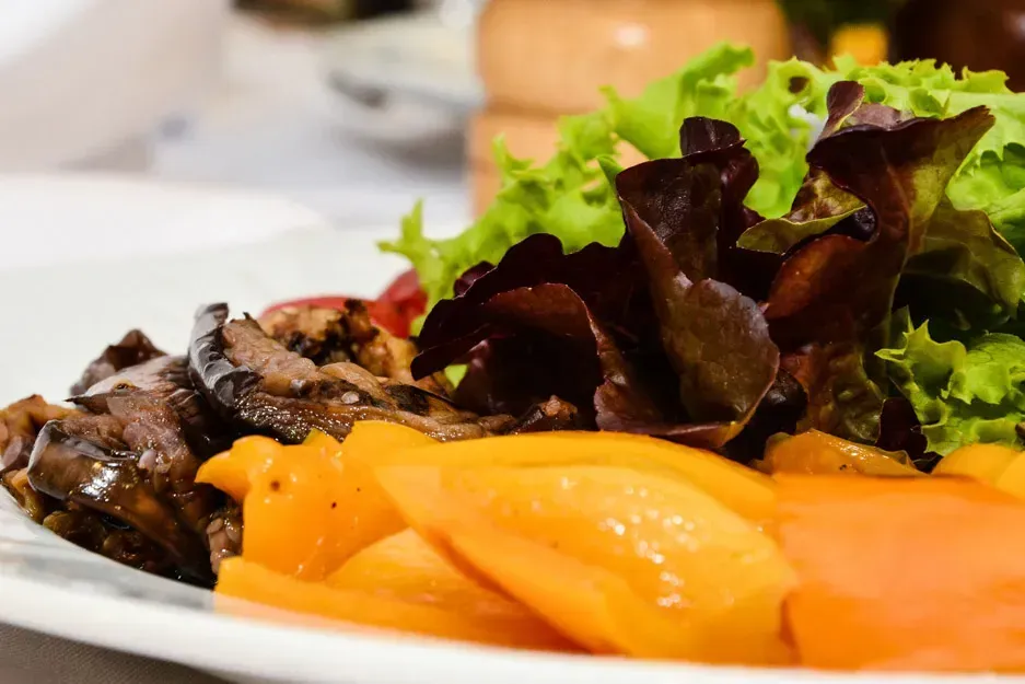 Elegantes Gericht mit gegrilltem Fleisch, orangefarbenen Paprikastreifen und frischem Salat auf weißem Teller – professionell