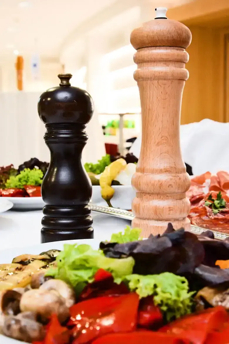 Elegante Foodfotografie Wien: Schwarzer Pfeffermühle und Holzsalzmühle neben frischen Zutaten wie Salat, Pilzen und Prosciutt