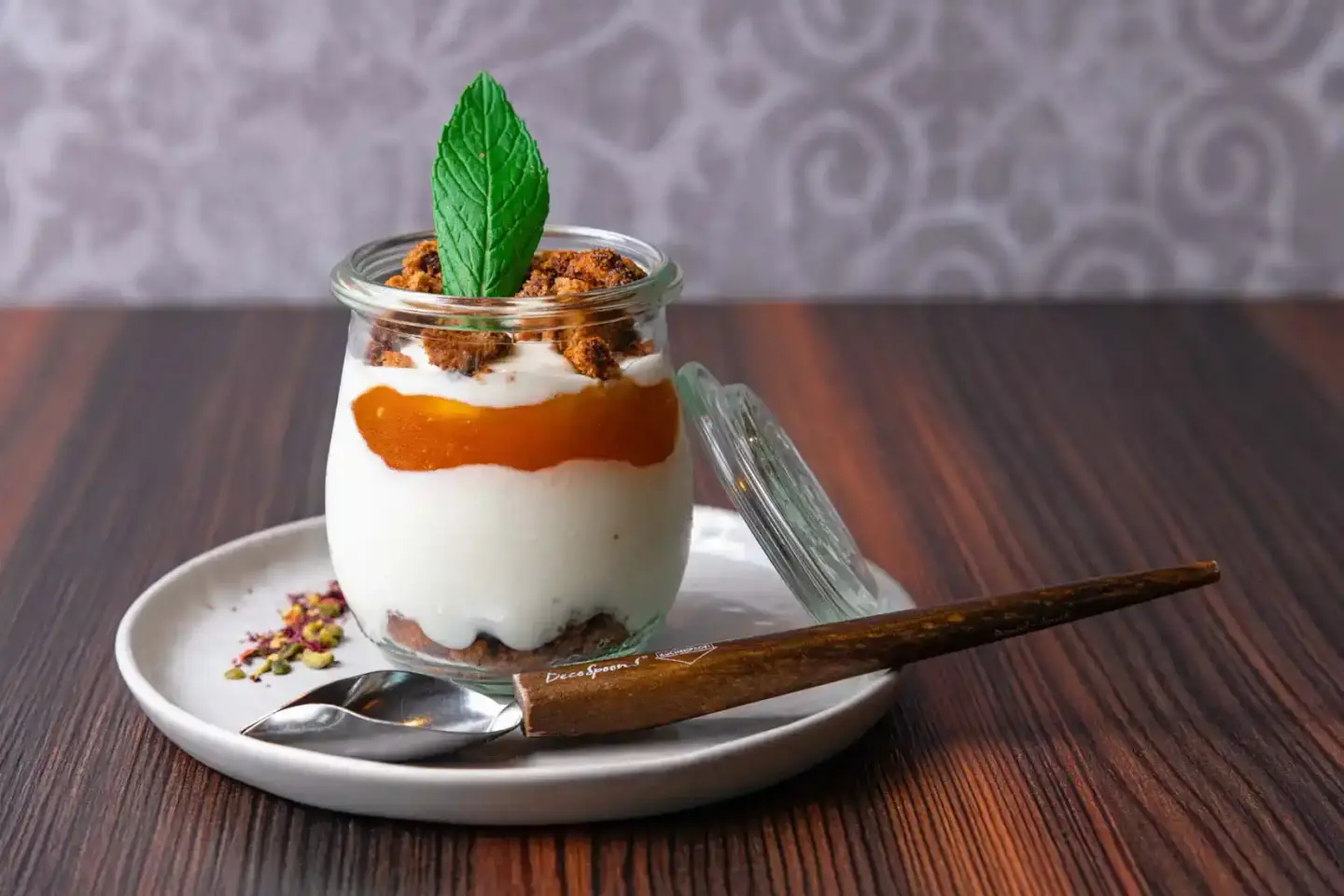 Elegantes Dessert im Glas mit Schichten aus Keks, Creme und Aprikosenkompott, garniert mit Minze und Krümeln - professionelle