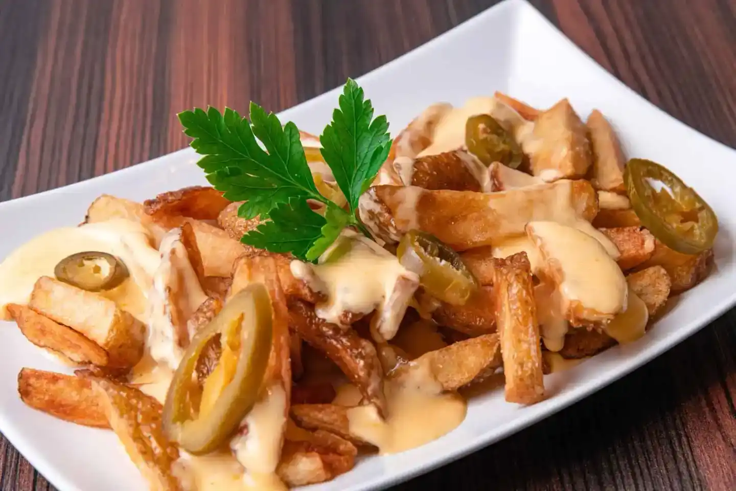 Knusprige Pommes mit Käsesauce und Jalapeños auf weißem Teller, professionelle Foodfotografie Wien